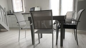 Una cuina moderna amb armaris blancs, una taula de dinar i caires. Hi ha un finestral amb un cortina de puntes i un microones al taulell.