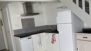 Una cuina compacta amb armaris blancs, un rentaplats, un frigorífic i una escala de fusta que condueix a una planta superior.