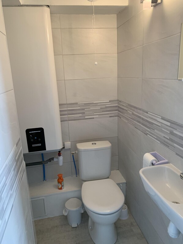 A modern bathroom with a toilet, bidet, sink, and a water heater. - T3 SEA and shops (Les Sables-d'Olonne)