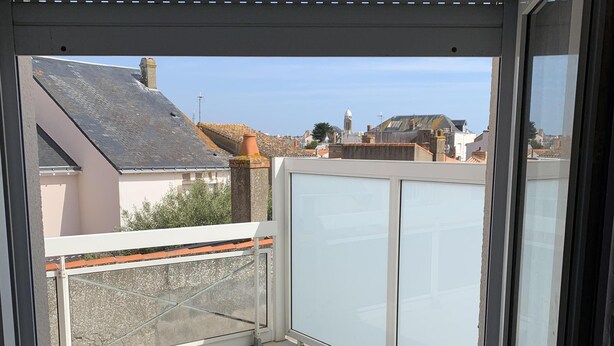 Un balcó amb una porta de vidre, un paviment de rajoles blanques i vista cap a edificis veïnals.