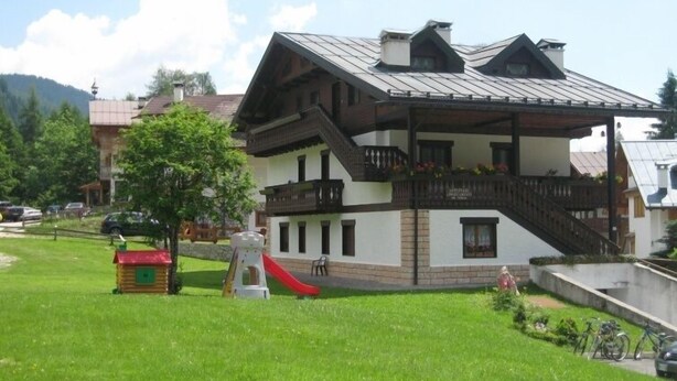 Un chalet a due piani con un balcone, uno scivolo rosso e una casetta dei giochi nel giardino.