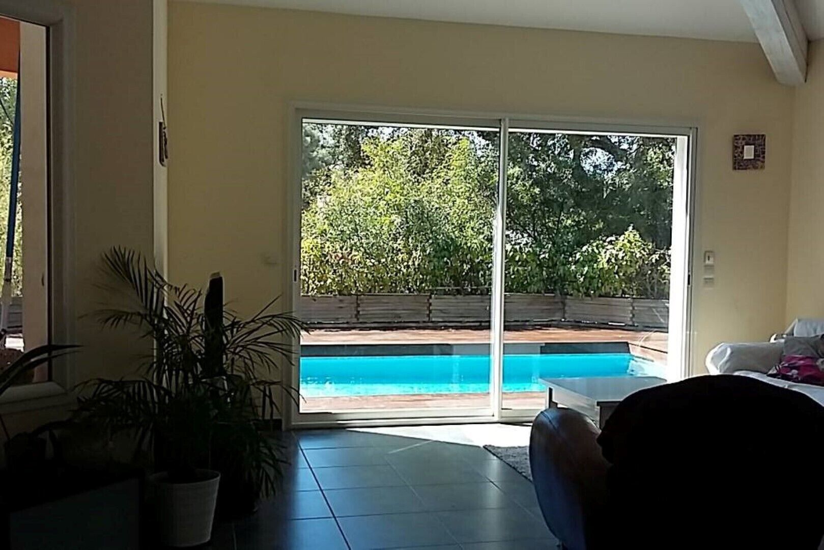 A room with a large sliding glass door leading to an outdoor swimming pool, surrounded by greenery.