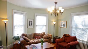 A living room with a brown sofa, a red armchair, a coffee table with magazines, and a chandelier. - A Village Bed and Breakfast (Newton)