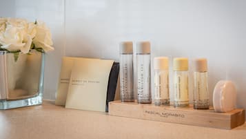 Une collection de produits de beauté disposée sur un plateau en bois, accompagnée d'une étiquette, d'un bonnet de douche et d'un vase contenant des fleurs blanches.
