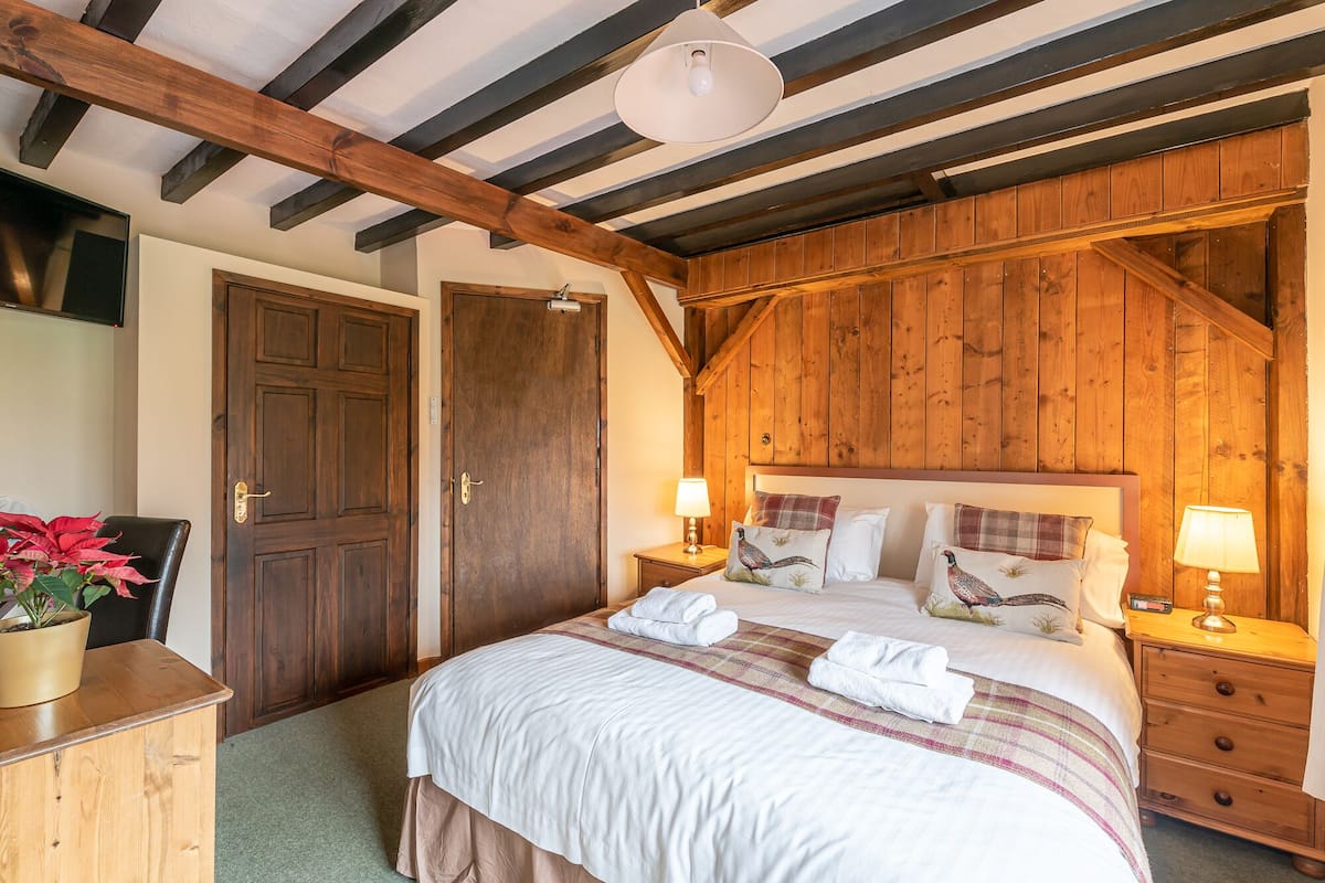 A bedroom with a wooden ceiling, a large bed with white bedding, two bedside tables with lamps, and a wooden wardrobe.
