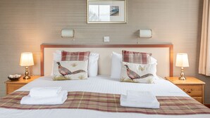 A hotel room with a large bed, two bedside lamps, a framed picture above the bed, and a checkered throw blanket. - The Fox and Hounds (Whitby)