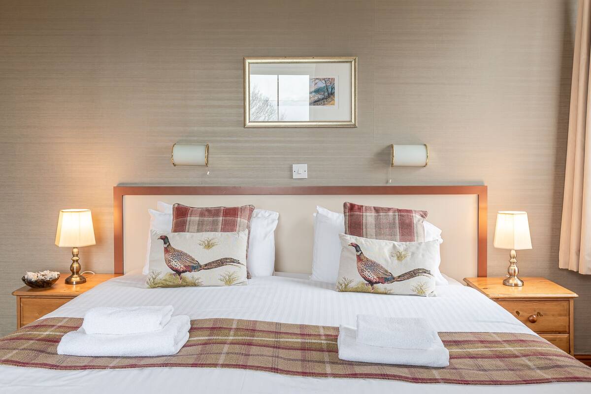 A hotel room with a large bed, two bedside lamps, a framed picture above the bed, and a checkered throw blanket.