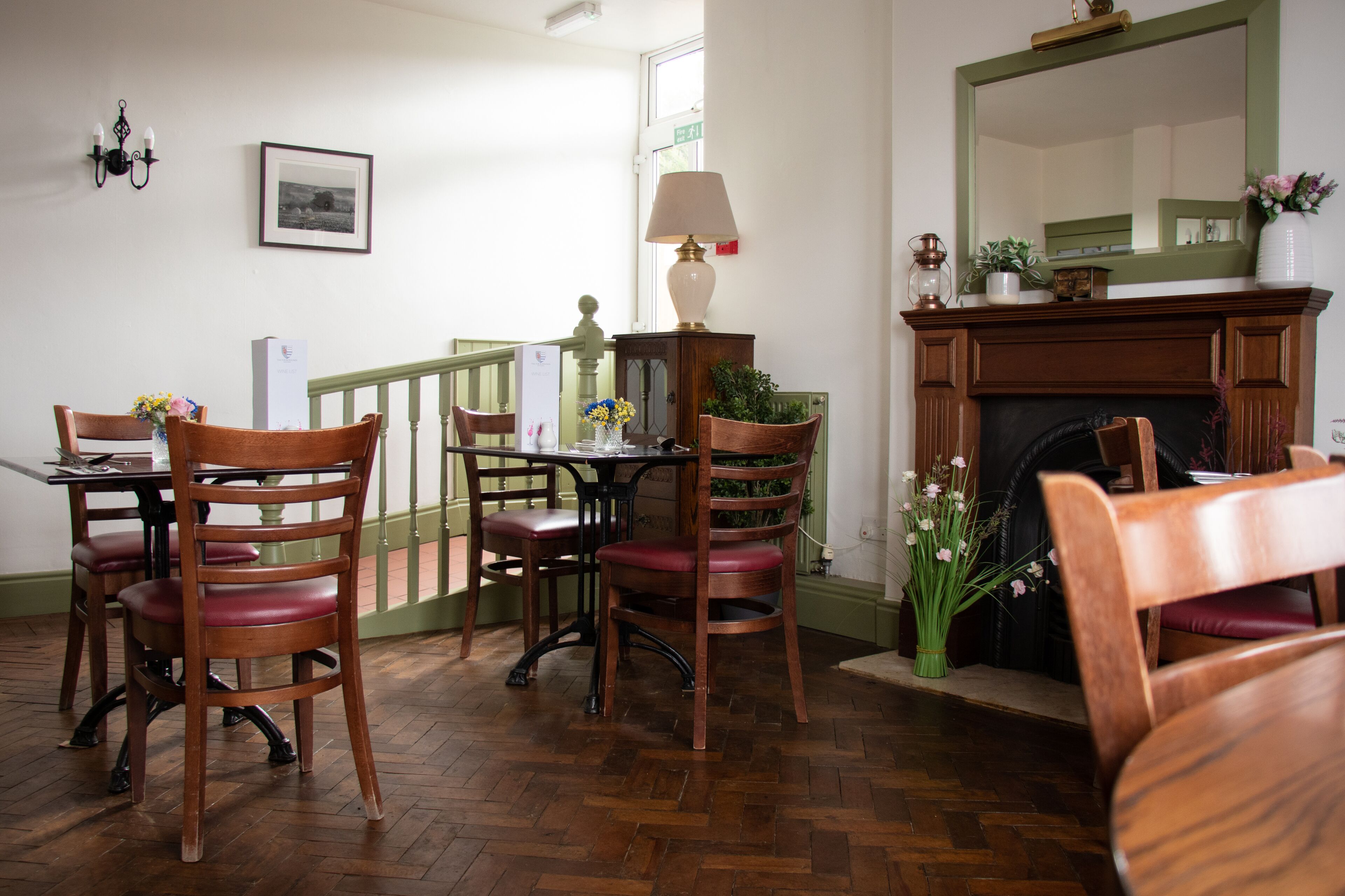 Een eetruimte met houten stoelen en een tafel, een open haard en een spiegel aan de muur.