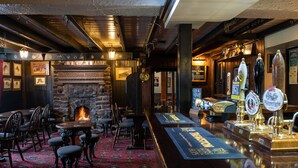 A bar area with a stone fireplace, wooden chairs, and a bar counter with various taps. - The Fox and Hounds (Whitby)