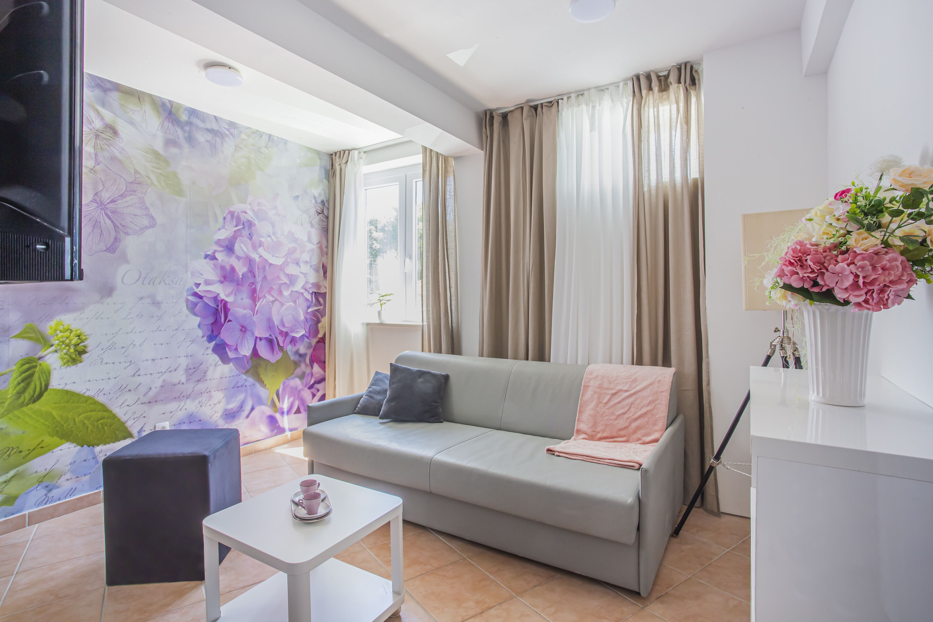 A modern living room with a sofa, a small table with cups, a decorative wall, and a window with curtains.