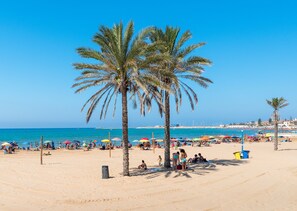 Een strand met palmbomen, parasols en mensen.