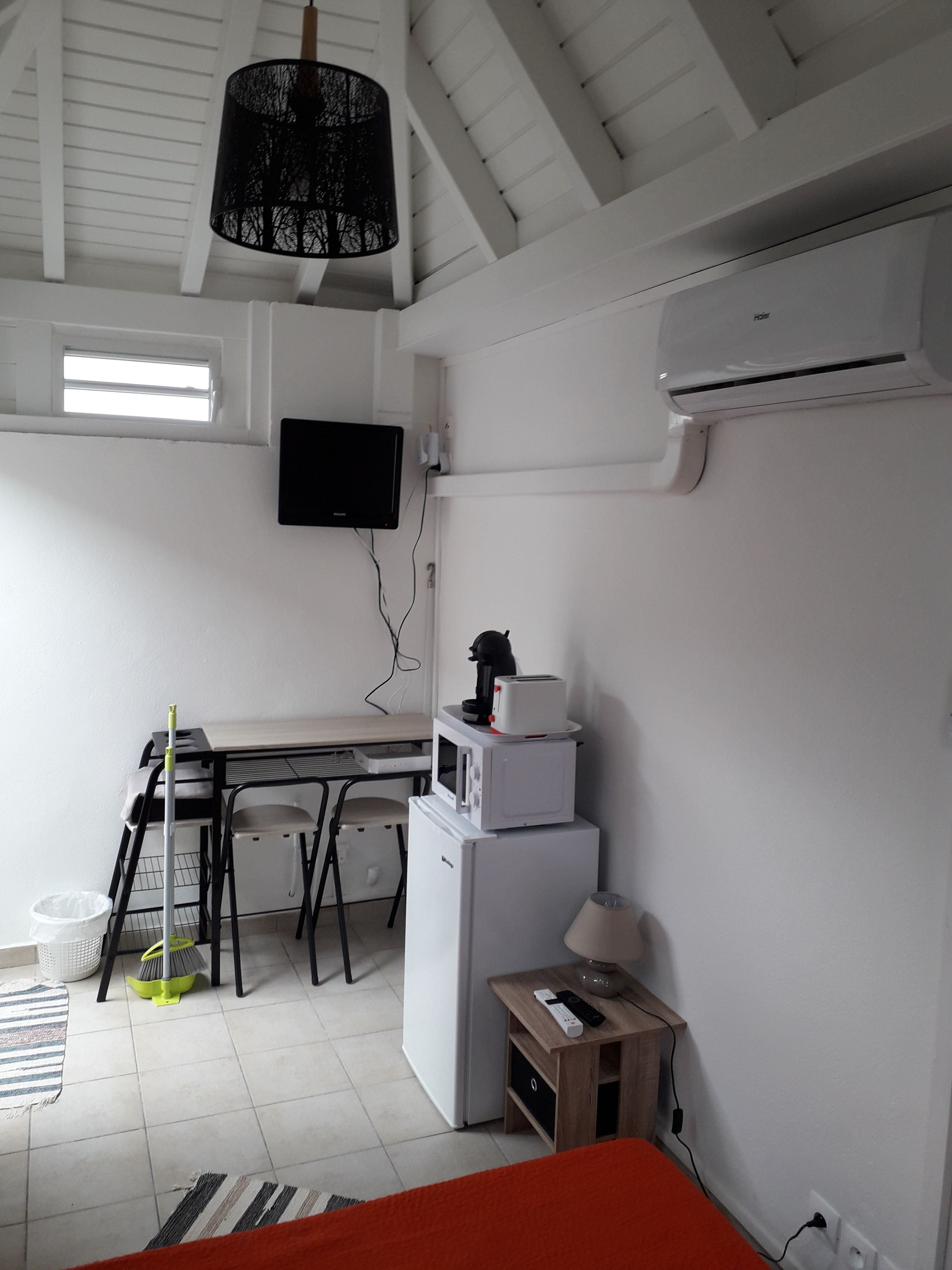 A compact room with a kitchenette, a bed, a TV mounted on the wall, and a ceiling fan.