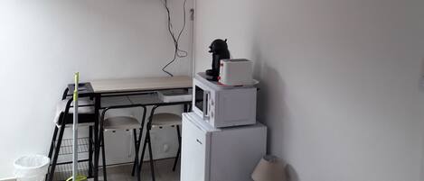 A compact room with a kitchenette, a bed, a TV mounted on the wall, and a ceiling fan.