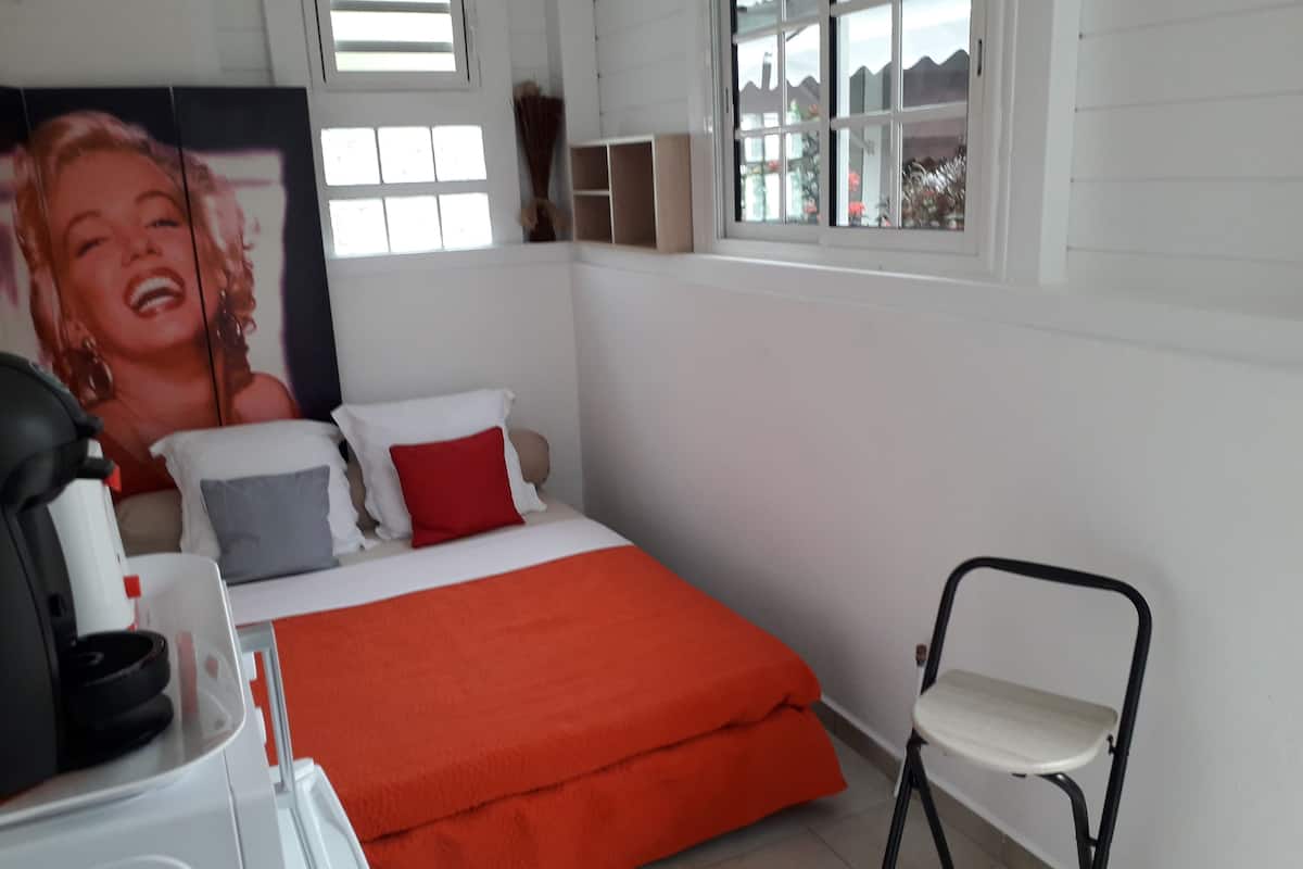 A bedroom with a bed, a chair, a desk, and a window.