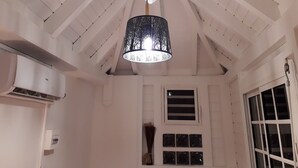 A room with a sloped ceiling, a hanging black chandelier, a white air conditioning unit, and a window with a view. - Le Saint Georges (Le Gosier)