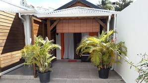 A covered patio area with two potted palm plants, a tiled floor, and a wooden building entrance. - Le Saint Georges (Le Gosier)