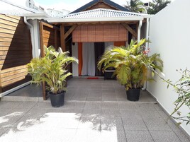Un patio techado con dos palmeras en macetas, suelo de baldosas y entrada de madera a un edificio.