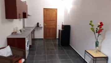 Een smalle gang met een keuken aan één kant, een houten deur aan het einde en een kleine tafel met een bloemenvaas aan de andere kant.