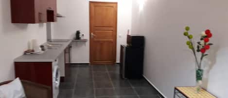 Un pasillo estrecho con una zona de cocina en un lado, una puerta de madera al final y una pequeña mesa con un jarrón de flores en el otro lado.