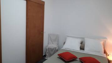Quarto pequeno e bem organizado, com uma cama, duas almofadas, uma mesa de cabeceira e uma porta de madeira.