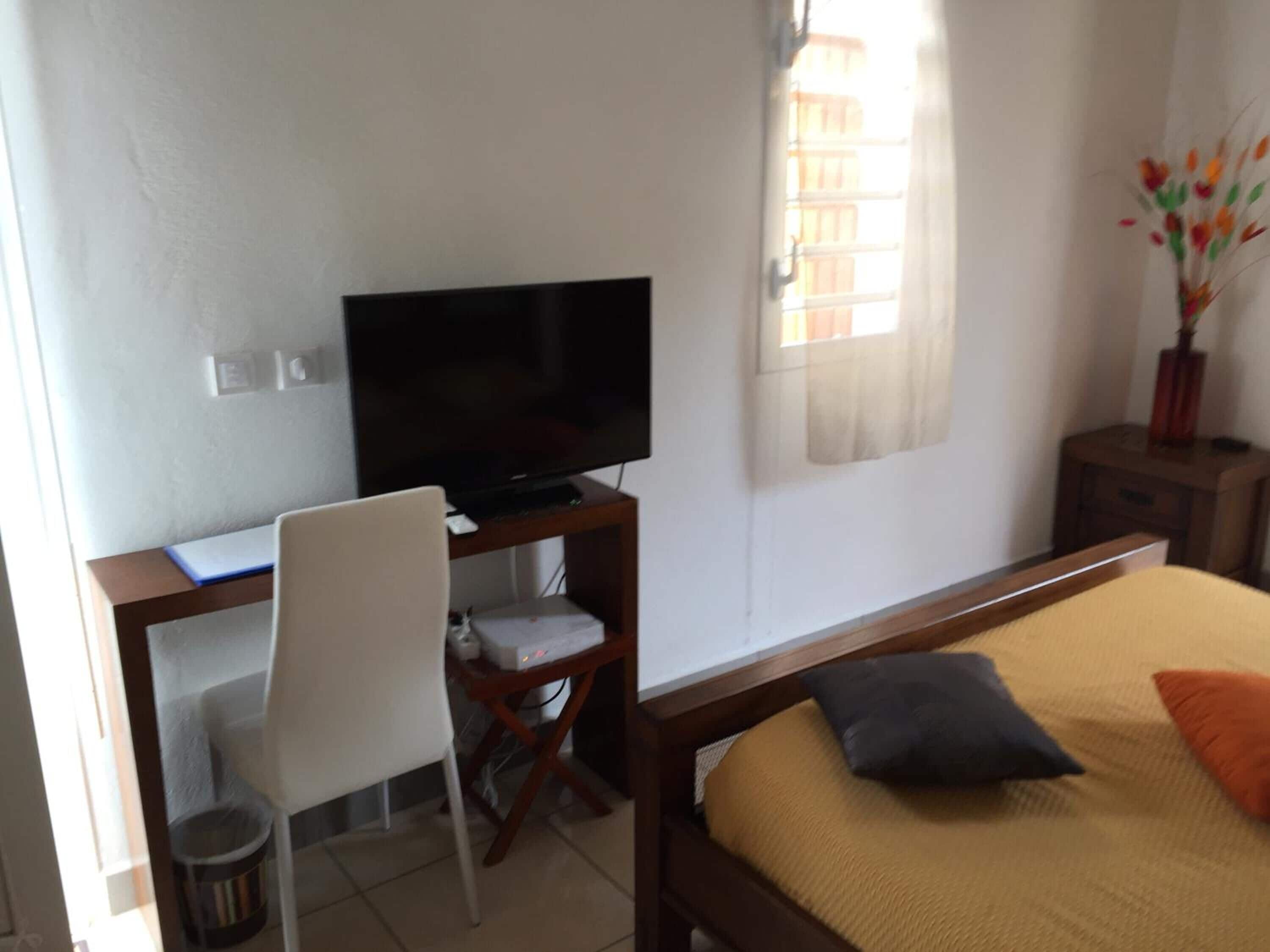 A bedroom with a bed, a desk with a television, a chair, and a small trash bin.