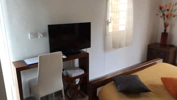 A bedroom with a bed, a desk with a television, a chair, and a small trash bin.