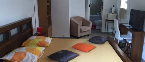 A hotel room with a bed, a chair, a desk, a television, and a bathroom visible through an open door.