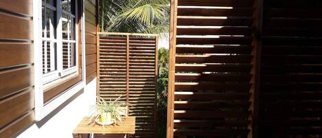 A wooden outdoor seating area with a table and chairs, a wooden fence, and a window.
