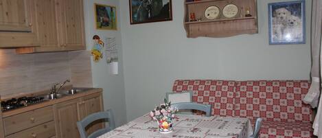 Una cocina con armarios de madera, un fregadero y una estufa. Hay una mesa de comedor con mantel a cuadros y sillas.