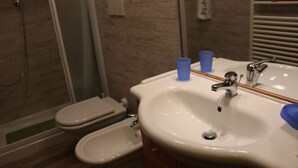 A bathroom with a white sink, a mirror, a shower, and a toilet. - Casa Bel Prà (Val di Zoldo)