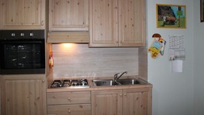 A kitchen with wooden cabinets, a stove, and a sink. - Casa Bel Prà (Val di Zoldo)