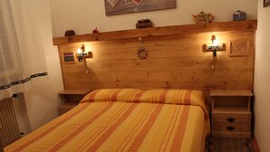 A bedroom with a wooden headboard, a striped bedspread, two bedside tables with lamps, and a small shelf with decorative items. - Casa Bel Prà (Val di Zoldo)