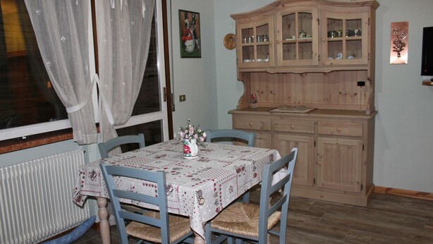 A dining area with a table set for four, surrounded by blue chairs. A wooden cabinet with glass doors is to the right. - Casa Bel Prà (Val di Zoldo)
