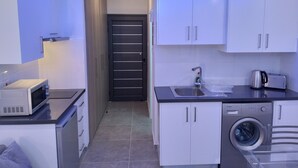 Una cocina compacta con armarios blancos, un microondas, un tostador y una lavadora.