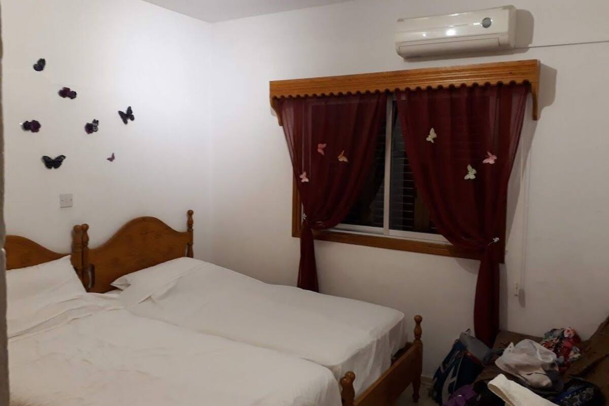 Ein Schlafzimmer mit einem hölzernen Bett, einem Fenster mit roten Vorhängen und Wandstickern mit Schmetterlingsmotiven.