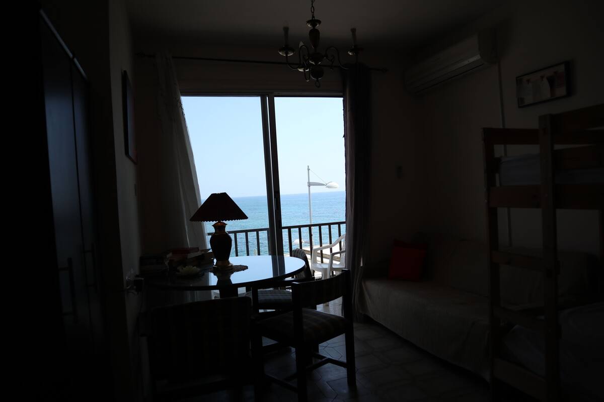 Ein Zimmer mit Esstisch und Stühlen, einer Couch und Meerblick durch ein großes Fenster.
