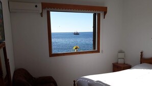 Un dormitorio con un ventanal grande que da al mar, una cama, una mesita de noche y una silla.