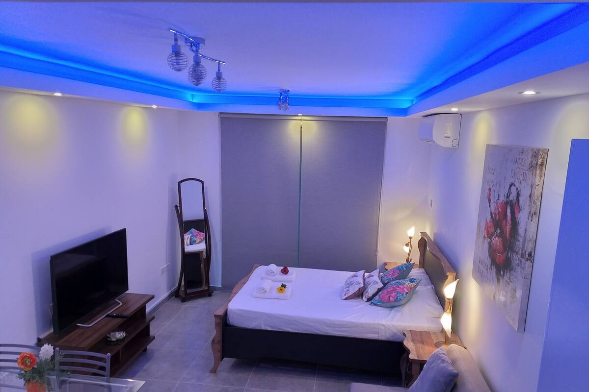 Ein modernes Schlafzimmer mit Bett, Nachttisch, Fernseher und einem Wandbild.