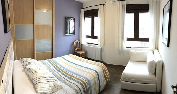Un dormitorio con cama, una silla, un sofá, una ventana y un radiador.