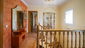Un pasillo con una escalera de madera, un candelabro y un espejo.