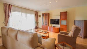 Una sala de estar con un sofá, sillones, una mesa de centro, un televisor y un mueble aparador.