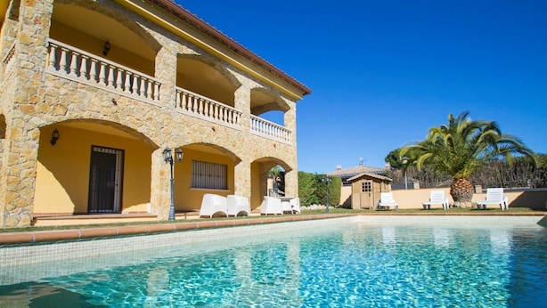 Un edificio de piedra con piscina, mobiliario exterior y palmeras.