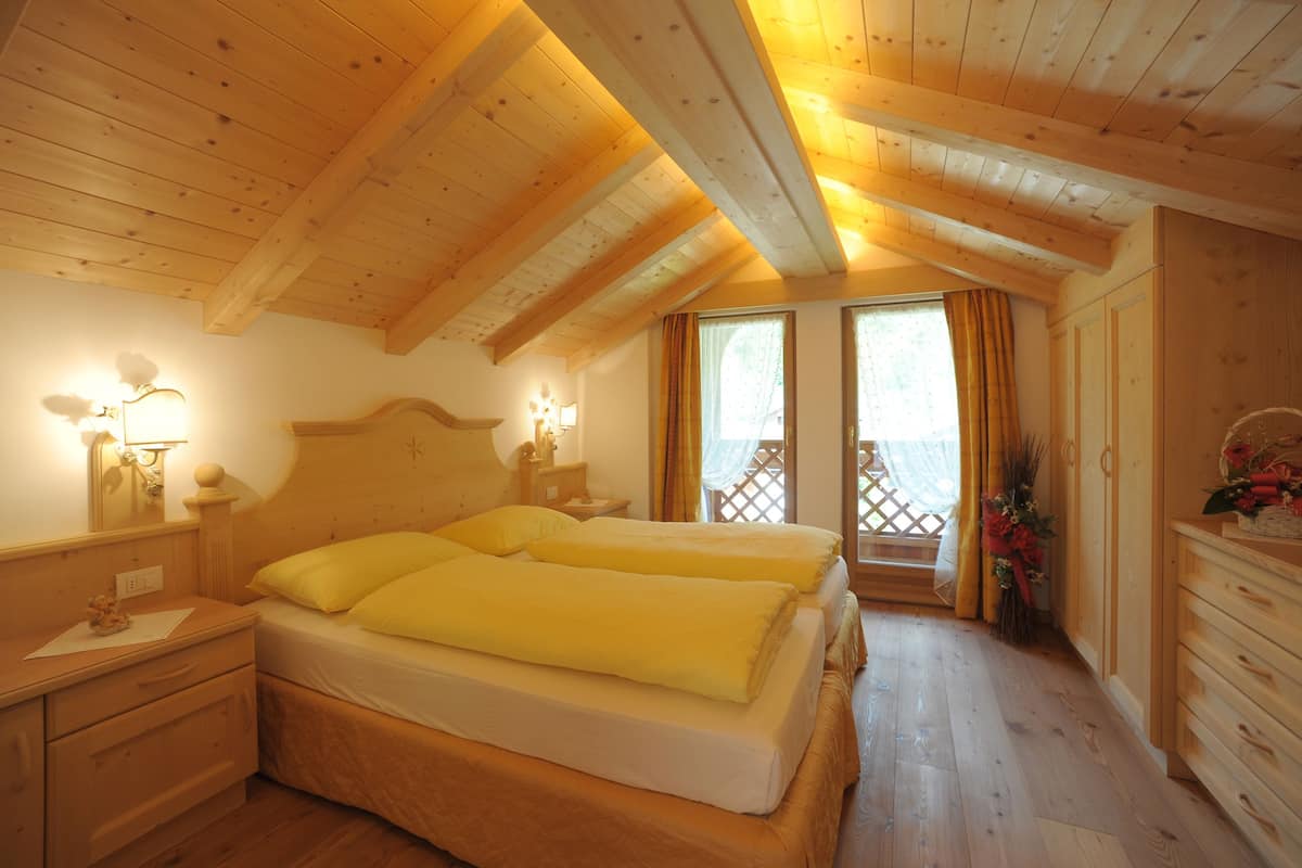 A wooden room with two beds, a nightstand, a dresser, and a window with curtains.