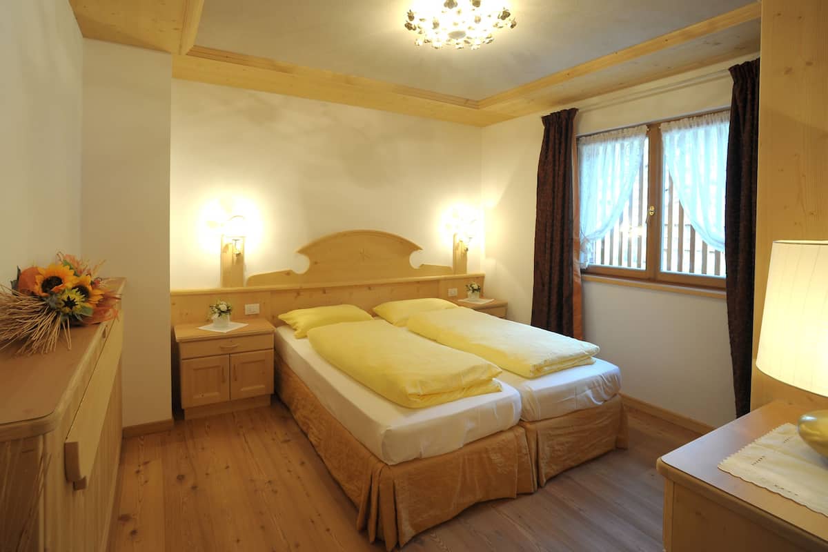A room with a wooden bed, two bedside tables, a nightstand, a lamp, and a window with curtains.