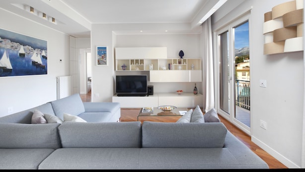 Ein modernes Wohnzimmer mit grauem Sofa, einem Flachbildfernseher und einem Glastisch.
