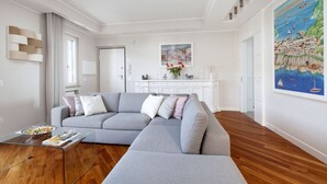 Ein modernes Wohnzimmer mit einem grauen Ecksofa, einem Glastisch und Holzboden.