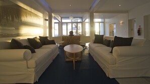 A modern living room with two white sofas, a round coffee table, and a large abstract painting on the wall. - Hotel Tofo Mar (Tofo)