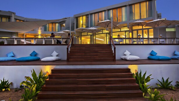 A modern hotel with a wooden staircase leading to a seating area with umbrellas. - Hotel Tofo Mar (Tofo)