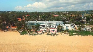 A beachfront property with a large building, a sandy beach, and palm trees. - Hotel Tofo Mar (Tofo)