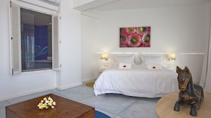 Un dormitorio con cama, una mesita de centro de madera con flores, una estatua decorativa de un caballo y un cuadro abstracto colorido en la pared.